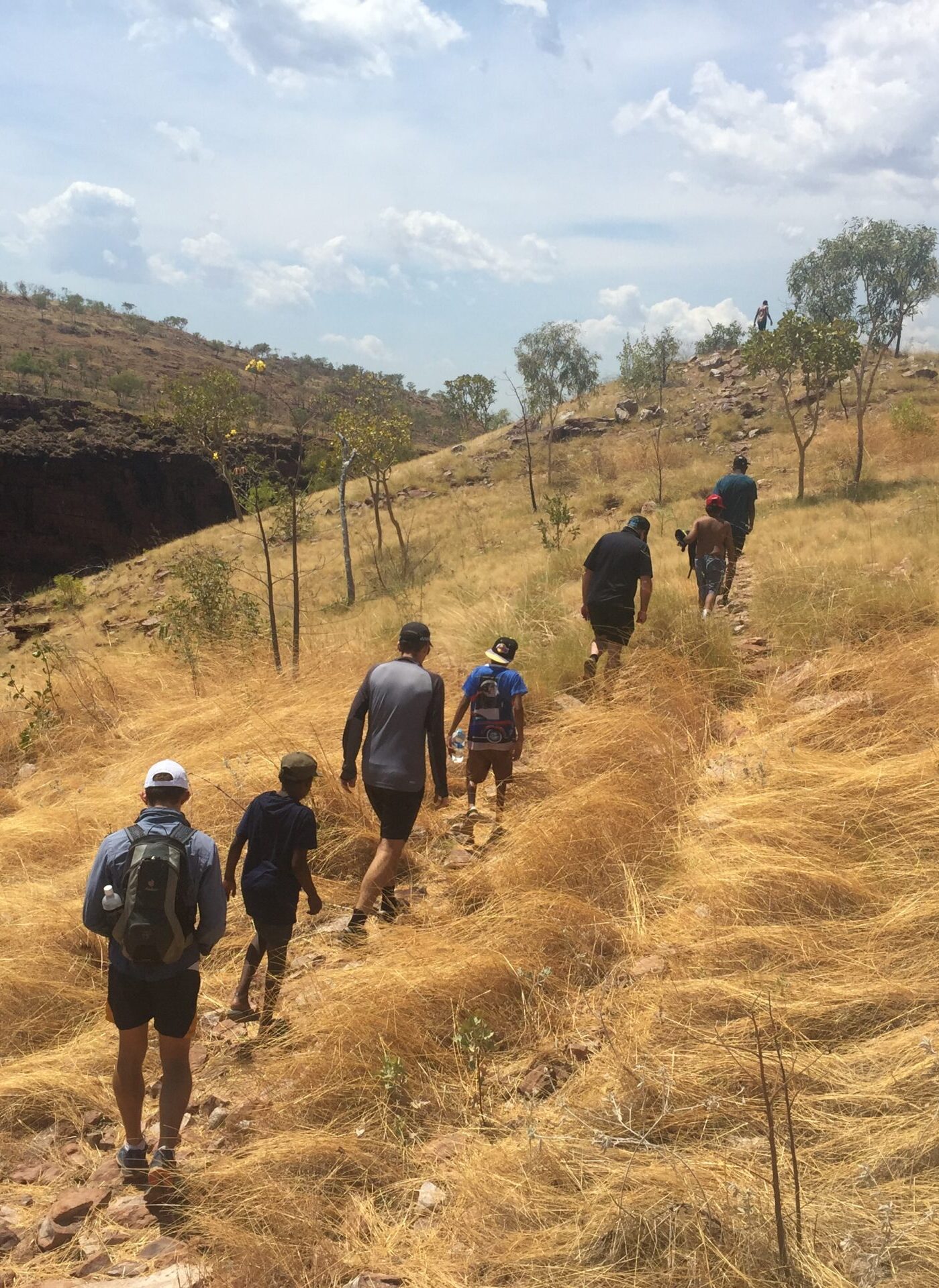 A group of Aboriginal men hiking up a grassy hill in the sun
